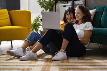 Happy women using laptop in living room - GIOF13511