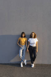 Young lesbian couple holding hands while standing on footpath - GIOF13517