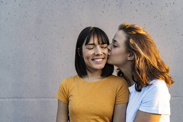 Girlfriend kissing woman in front of gray wall - GIOF13543