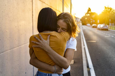 Frau umarmt Freundin auf der Straße bei Sonnenuntergang - GIOF13548