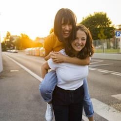 Happy woman giving piggyback ride to girlfriend on road - GIOF13565