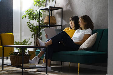 Smiling lesbian couple sharing laptop in living room - GIOF13570