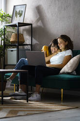 Glückliches lesbisches Paar, das einen Laptop benutzt, während es zu Hause sitzt - GIOF13571
