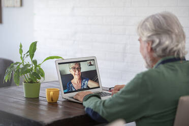 Man talking with senior woman through video on laptop call at home - SIPF02390