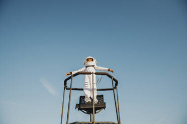 Boy wearing space suit standing with arms outstretched on chair - AANF00089