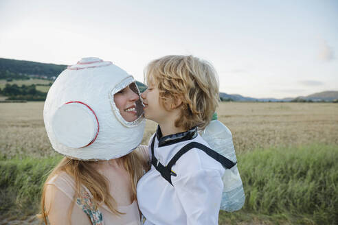 Lächelnde Mutter mit Weltraumhelm, die ihren Sohn auf dem Feld umarmt - AANF00104