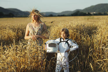 Mother standing with son wearing space suit at field - AANF00107