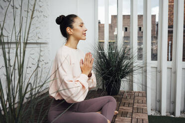 Frau mit verschränkten Händen übt Yoga auf der Terrasse - VPIF04980