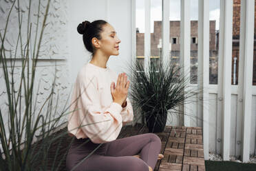 Woman with hands clasped practicing yoga on terrace - VPIF04980