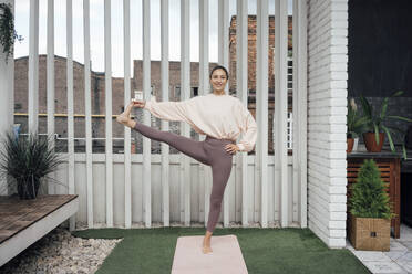 Lächelnde Frau beim Üben der Utthita Hasta Padangusthasana-Pose auf der Terrasse - VPIF04981