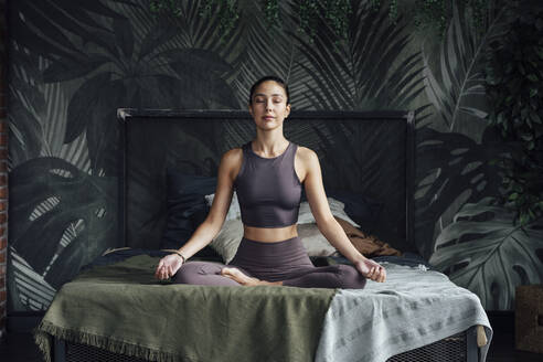 Mid erwachsene Frau mit geschlossenen Augen übt Yoga im Schlafzimmer zu Hause - VPIF04988