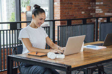 Lächelnde weibliche Fachkraft, die einen Laptop benutzt, während sie am Schreibtisch im Büro sitzt - VPIF04993