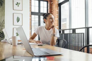 Thoughtful businesswoman with hand on chin sitting at desk - VPIF04998