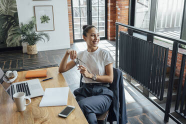 Smiling thoughtful female professional sitting at desk in office - VPIF05002