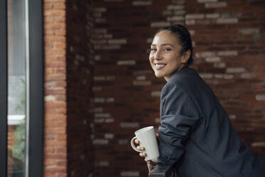 Smiling businesswoman with coffee cup in office - VPIF05010