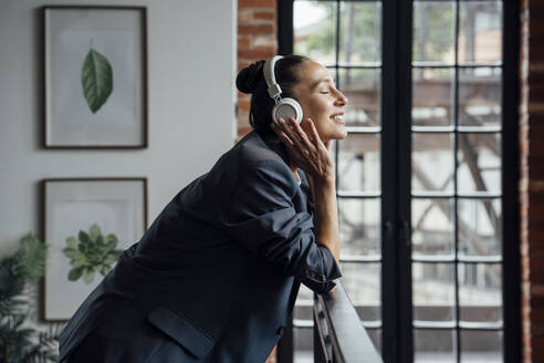 Mittlere erwachsene Geschäftsfrau hört Musik über Kopfhörer im Büro - VPIF05014
