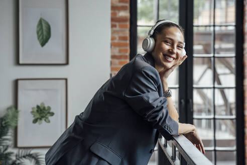 Glückliche Geschäftsfrau mit drahtlosen Kopfhörern im Büro - VPIF05015