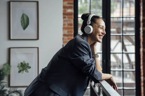 Glückliche Geschäftsfrau hört Musik über drahtlose Kopfhörer im Büro - VPIF05016