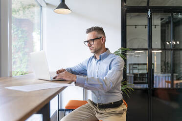 Geschäftsmann mit Laptop am Schreibtisch sitzend - OIPF01088