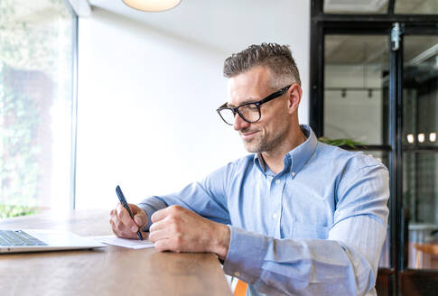 Male business professional writing on paper at desk in office - OIPF01092