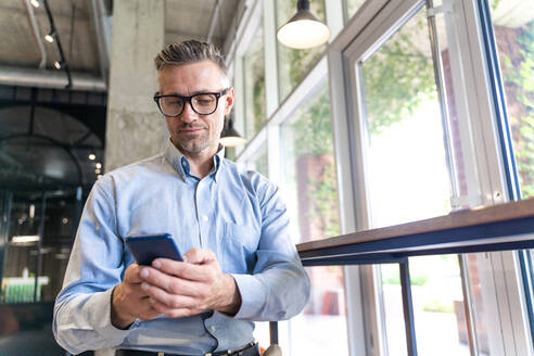 Älterer Geschäftsmann benutzt Smartphone am Arbeitsplatz - OIPF01095