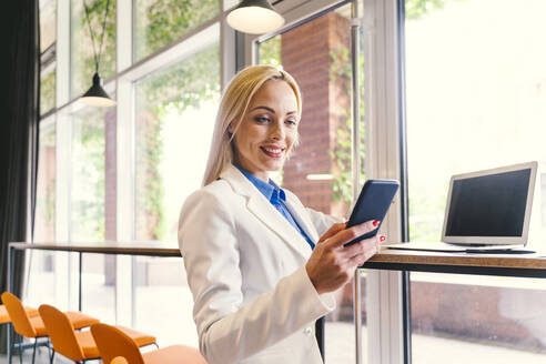 Blonde Geschäftsfrau benutzt Mobiltelefon am Arbeitsplatz - OIPF01099