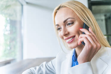 Lächelnde blonde Geschäftsfrau, die mit einem Smartphone im Büro spricht - OIPF01105