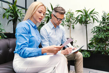 Female professional reading document while sitting by male colleague in office - OIPF01117