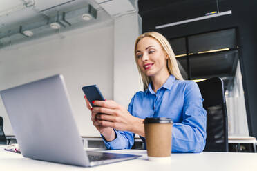 Female business professional using mobile phone while sitting with laptop in office - OIPF01150