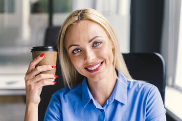 Blond businesswoman holding disposable cup in office - OIPF01153