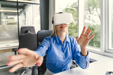 Smiling businesswoman wearing virtual reality headset at workplace - OIPF01161