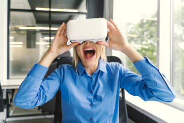 Glückliche Geschäftsfrau mit Virtual-Reality-Headset im Büro - OIPF01163