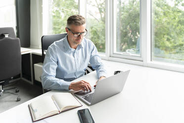 Männlicher Geschäftsmann, der einen Laptop bei der Arbeit im Büro benutzt - OIPF01165