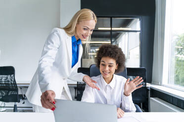 Lächelnde Geschäftsfrauen, die an einem Videoanruf über einen Laptop im Büro teilnehmen - OIPF01183