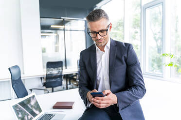 Männlicher Geschäftsmann mit Brille, der im Büro ein Smartphone benutzt - OIPF01204