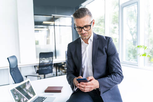 Männlicher Geschäftsmann mit Brille, der im Büro ein Smartphone benutzt - OIPF01204