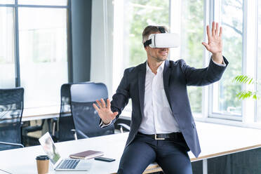 Geschäftsmann gestikuliert, während er ein Virtual-Reality-Headset im Büro trägt - OIPF01208