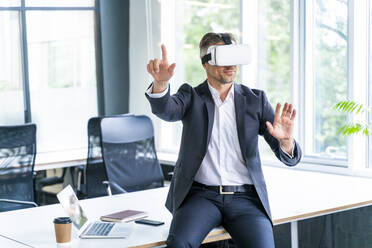 Male business professional wearing virtual reality headset gesturing in office - OIPF01209