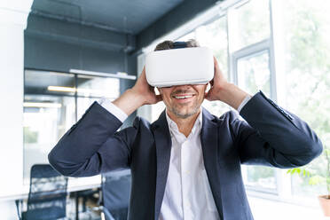 Smiling businessman wearing virtual reality headset in office - OIPF01210