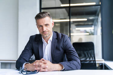 Male business professional with hands clasped sitting at desk in office - OIPF01214