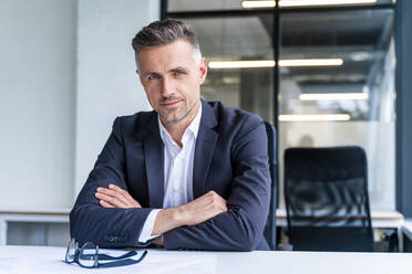 Businessman with arms crossed sitting at desk in office - OIPF01215