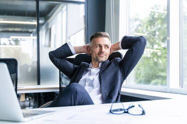 Mature business professional sitting with hands behind head relaxing in office - OIPF01220