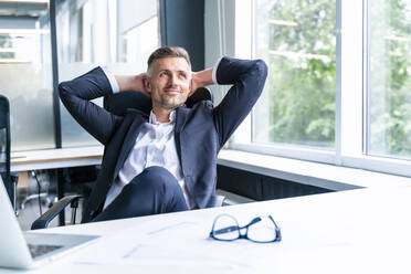 Thoughtful businessman with hands behind head relaxing in office - OIPF01221