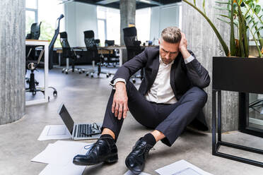 Geschäftsmann mit Kopf in der Hand sitzt auf dem Boden in einem Büro - OIPF01229