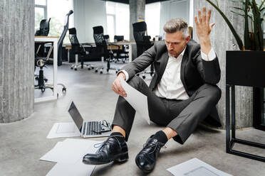 Frustrated businessman gesturing while looking at document in office - OIPF01230