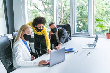 Männliche und weibliche Geschäftsleute tragen bei der Arbeit im Büro einen Mundschutz - OIPF01233