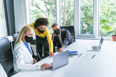 Male and female business professionals wearing protective face mask while working in office - OIPF01233