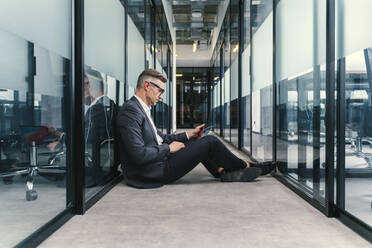 Businessman working on laptop while sitting in corridor at office - OIPF01257