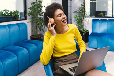 Carefree businesswoman singing while listening music through wireless headphones in office lobby - OIPF01271