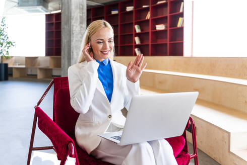 Weiblicher Geschäftsmann winkt während eines Videogesprächs auf dem Laptop im Büro - OIPF01300